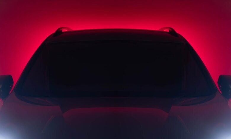 Close-up of a car's front end with a dark silhouette against a red background.