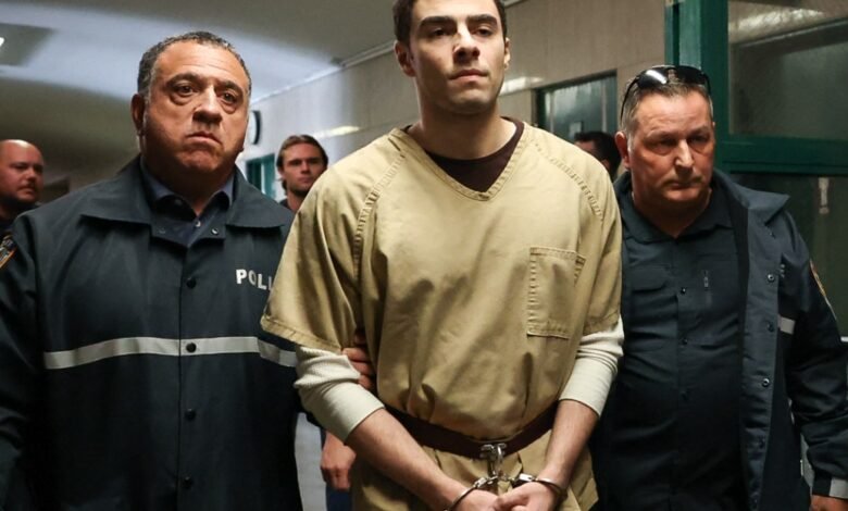 Man in prison uniform escorted by two police officers.