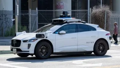 White Waymo self-driving car on city street with sensor equipment.