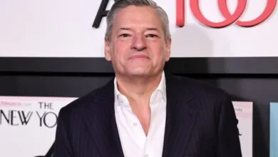 Gray-haired man in suit poses against 'The New Yorker' backdrop.