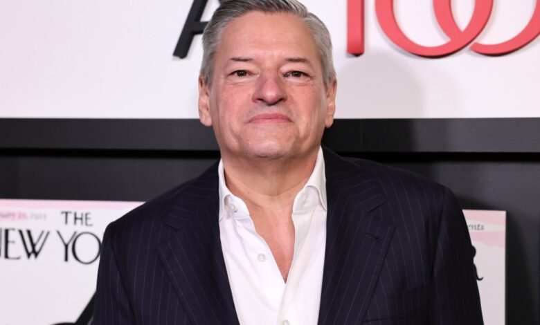 Gray-haired man in suit poses against 'The New Yorker' backdrop.