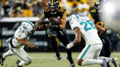 Football player #30 runs with the ball, pursued by two defenders.