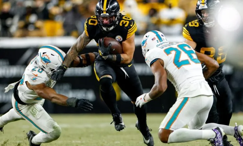 Football player #30 runs with the ball, pursued by two defenders.