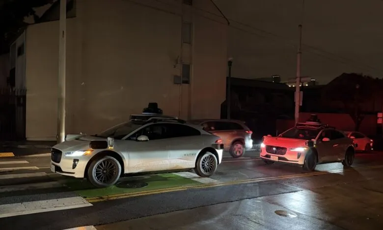 Two Waymo self-driving cars on a city street at night.