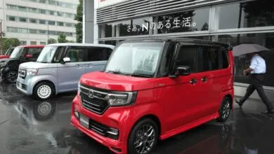 Row of colorful Honda N-Box kei cars parked outside on a rainy day.
