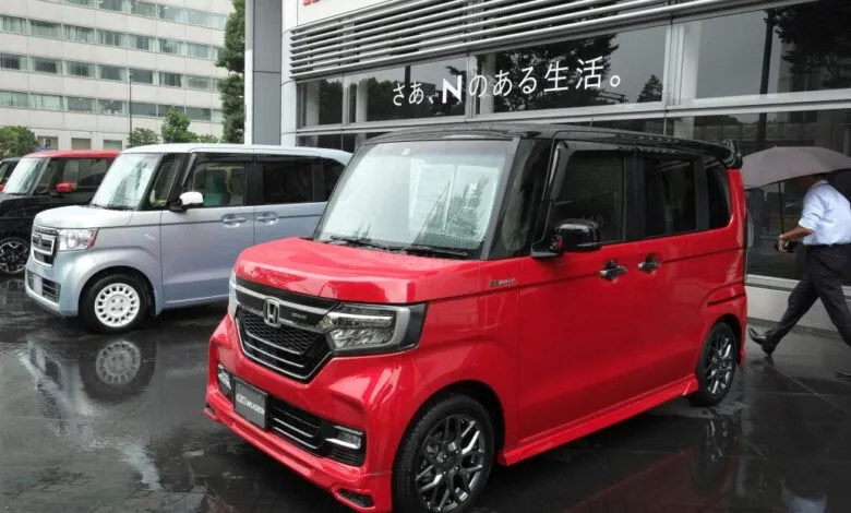 Row of colorful Honda N-Box kei cars parked outside on a rainy day.