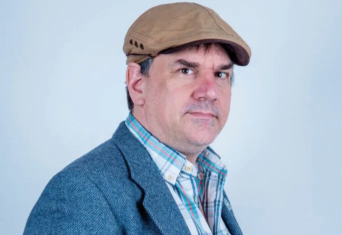 Portrait of a man wearing a tweed jacket and a cap.