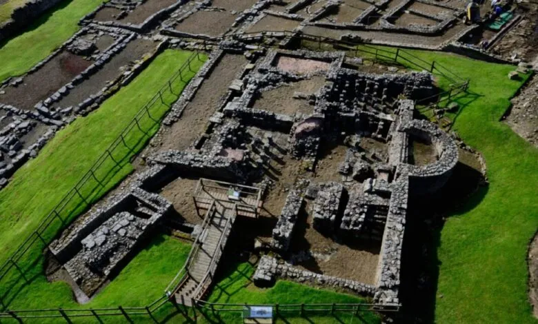 Aerial view of Roman fort ruins with stone walls and green grass.