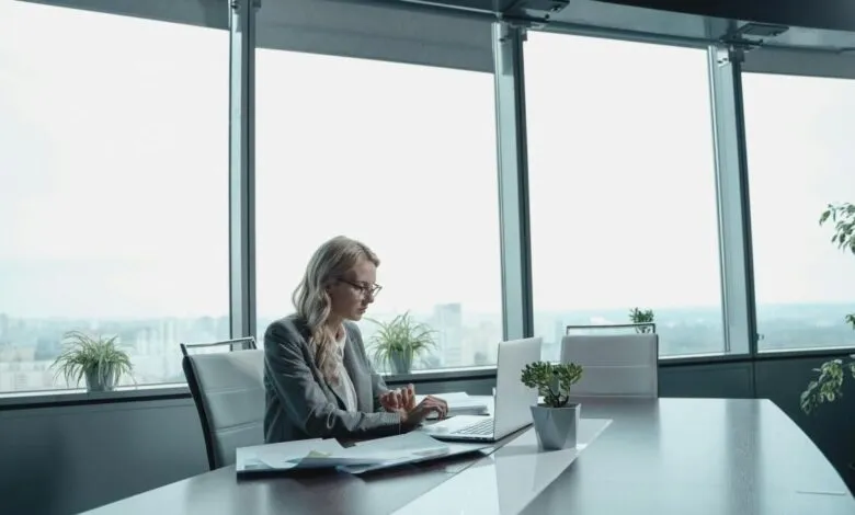 Businesswoman working on laptop in modern office with city view.