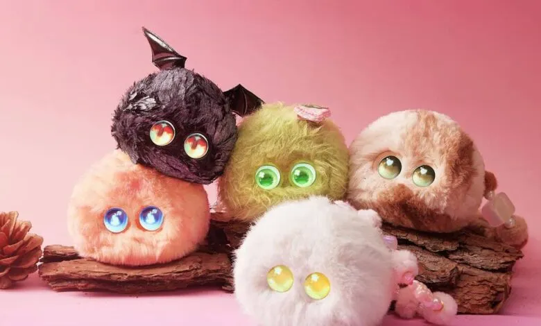 Five colorful, fluffy plush toys with large eyes on a piece of bark.