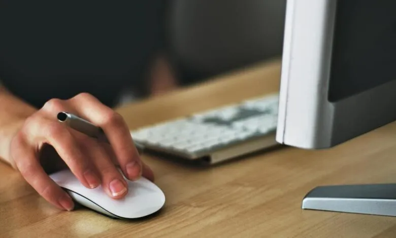 Hand using a computer mouse with a pen held between fingers.