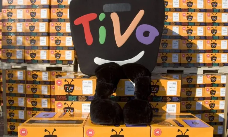 TiVo mascot surrounded by stacks of TiVo boxes on pallets.