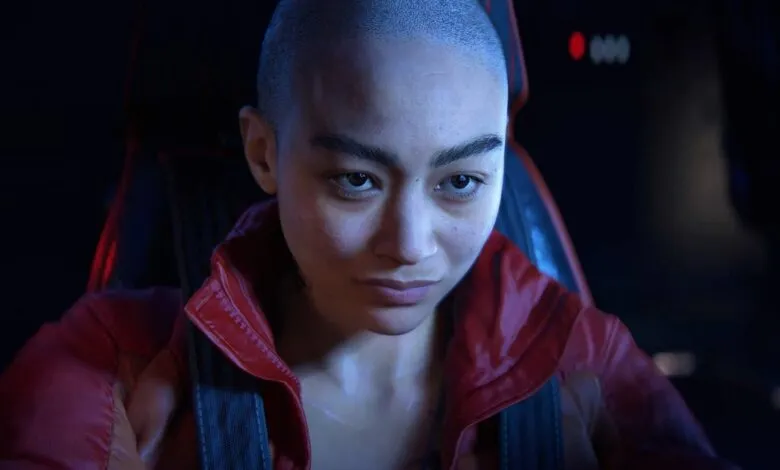 Close-up of a woman with a shaved head in a red jacket, looking intently.