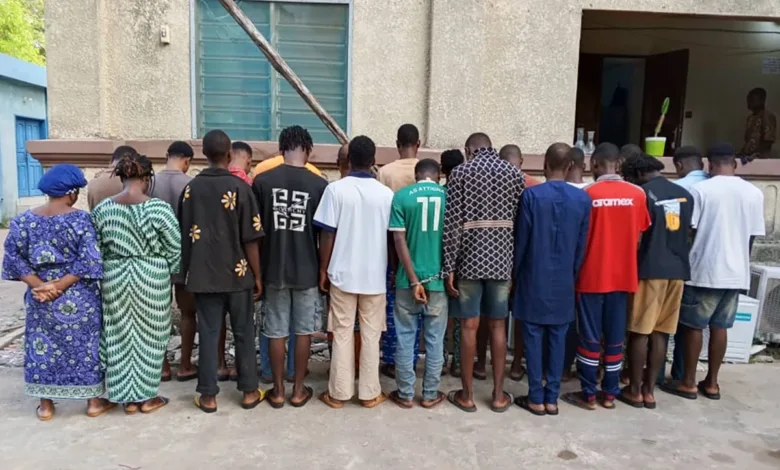 Group of people standing with their backs to the camera, one in handcuffs.