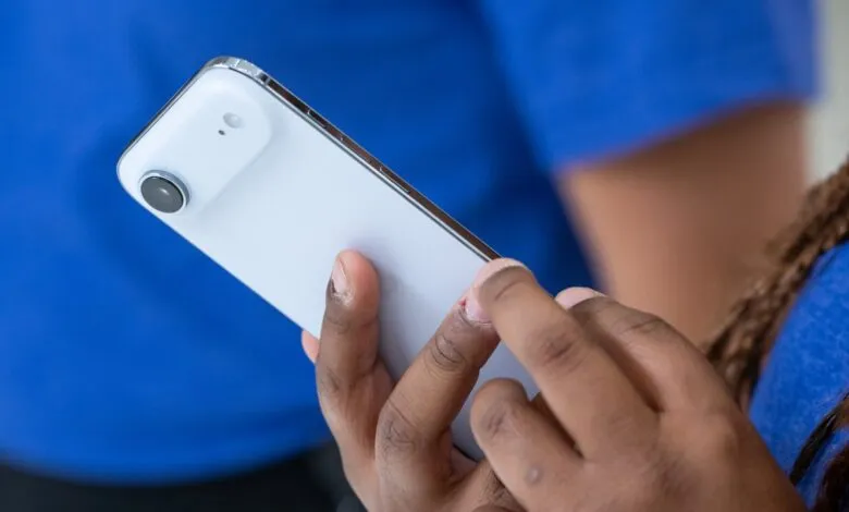 Person holding a white smartphone with a prominent camera module.