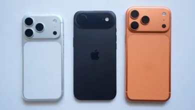 Three iPhones in silver, black, and orange, showcasing their rear designs.