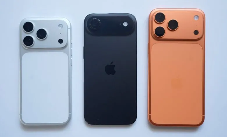 Three iPhones in silver, black, and orange, showcasing their rear designs.