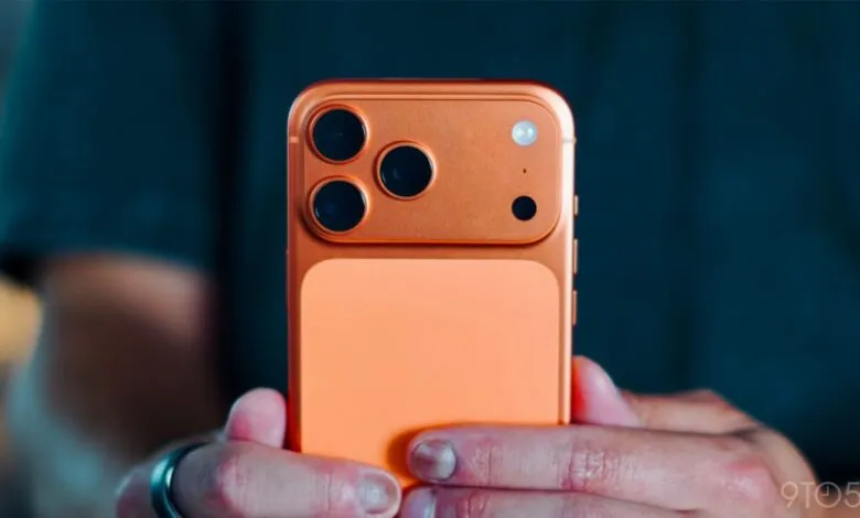 Orange smartphone with triple camera system held in hands.