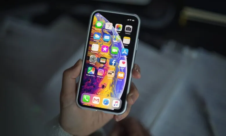 Hand holding iPhone with app icons visible on the screen.
