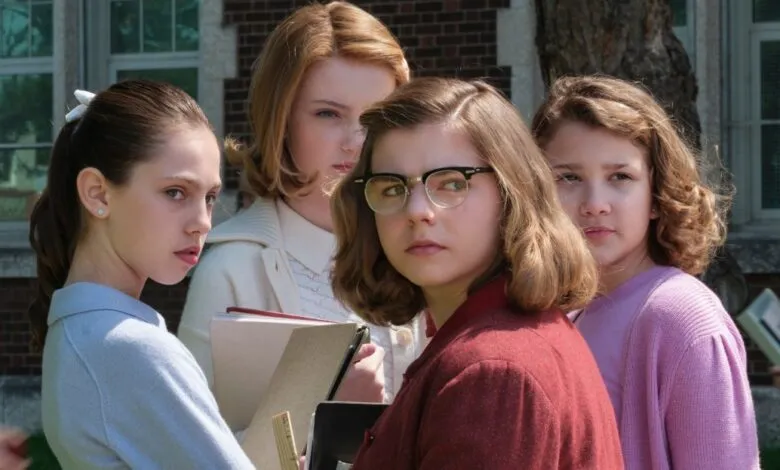 Four young women stand together, looking serious and thoughtful.