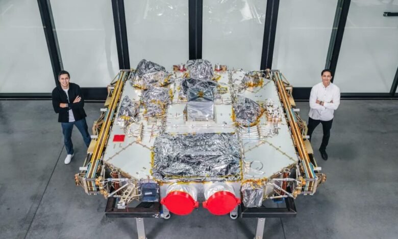 Two men stand beside a spacecraft component, showcasing its size and complexity.