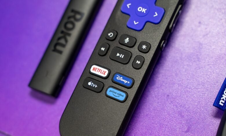 Roku remote with streaming service buttons on a purple surface.