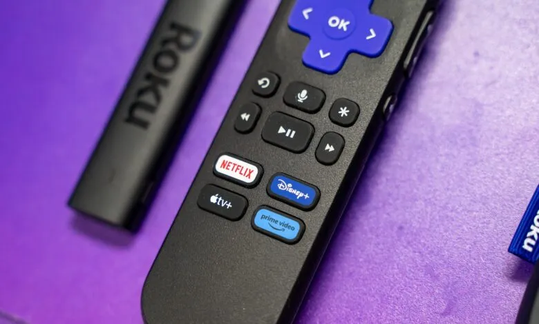 Roku remote with streaming service buttons on a purple surface.