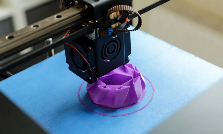 3D printer creating a purple geometric object on a blue surface.