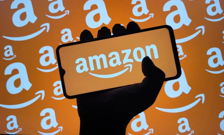 Hand holds phone displaying Amazon logo against Amazon-branded background.