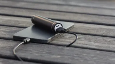 Black power bank charging a gray smartphone on a wooden surface.