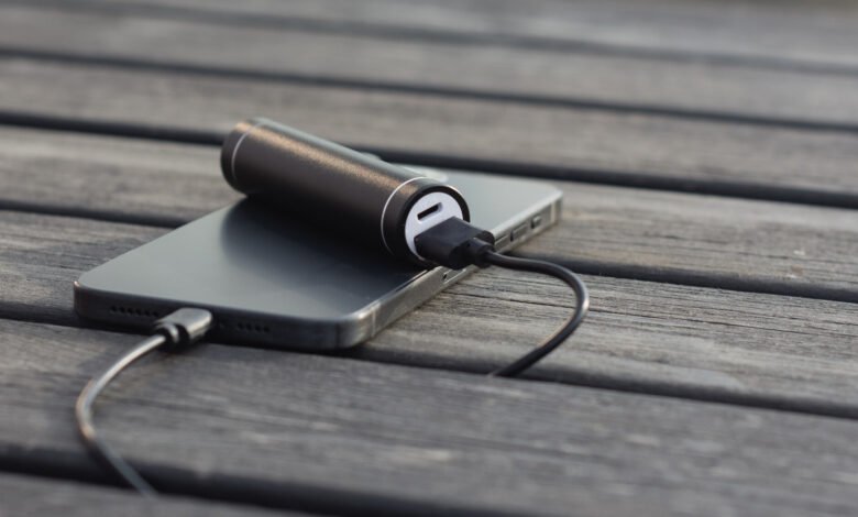 Black power bank charging a gray smartphone on a wooden surface.