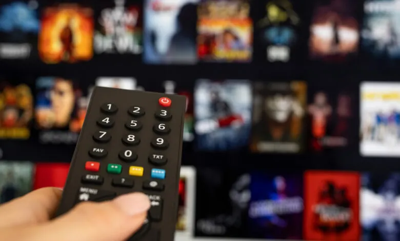 Hand holding remote control in front of streaming service interface.