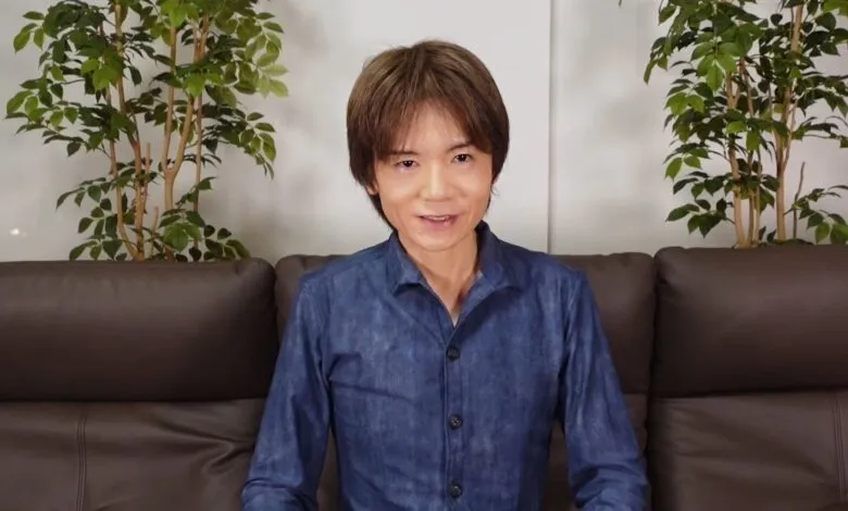 Masahiro Sakurai sits on a brown couch, smiling at the camera.
