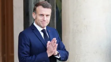 Emmanuel Macron with hands clasped, wearing a navy suit.