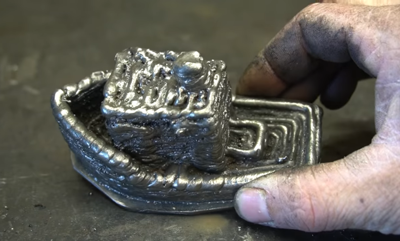 Metal 3D printed Benchy boat held by a dirty hand.