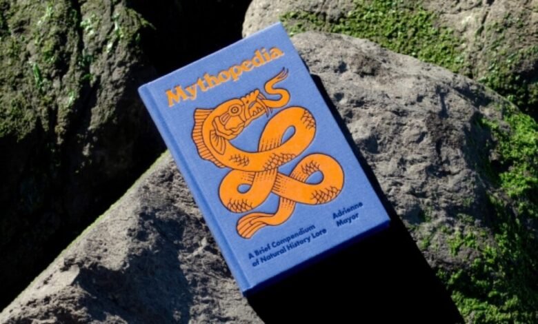 Book 'Mythopedia' by Adrienne Mayor on mossy rocks, orange dragon.