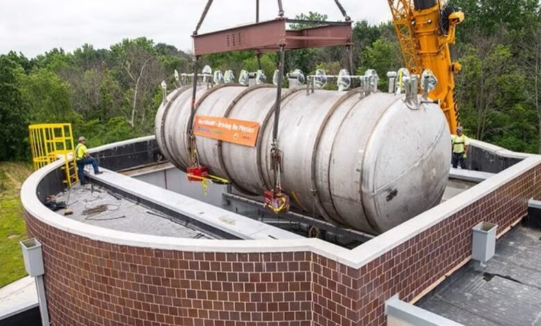 Large cylindrical detector being lowered into a brick-lined pit by a crane.
