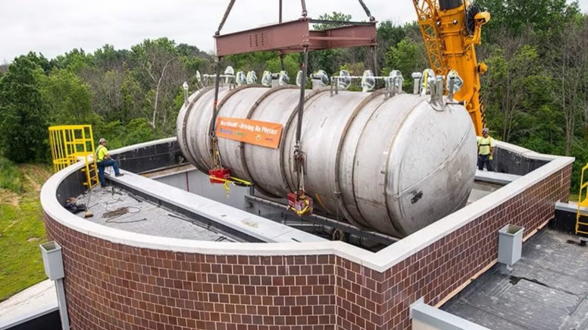 Large cylindrical detector being lowered into a brick-lined pit by a crane.