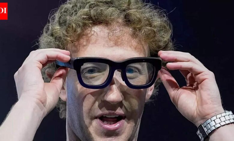 Man with curly hair adjusts black-framed glasses, looking forward.