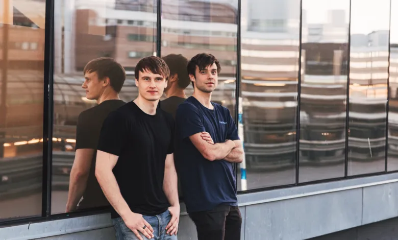 Two young men stand against a glass building, reflected in the glass.