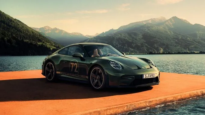 Green Porsche 911 GT3 parked on a dock with mountains and lake in the background.