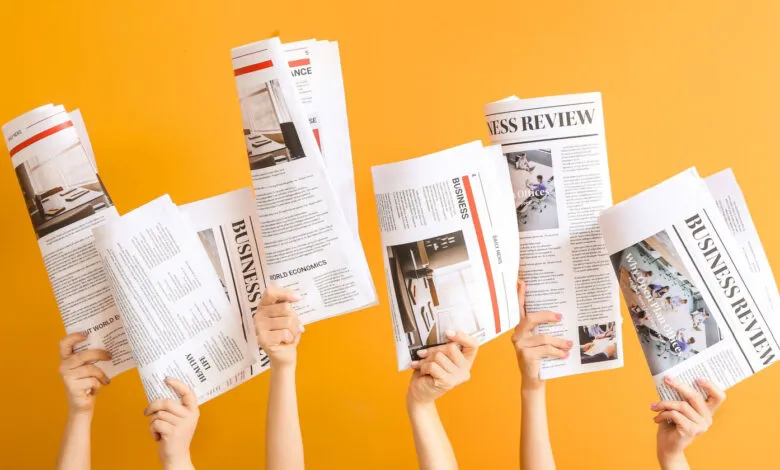 Hands holding business newspapers against a bright orange background.