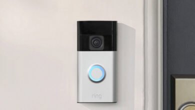 Ring video doorbell mounted on a white wall next to a dark door.