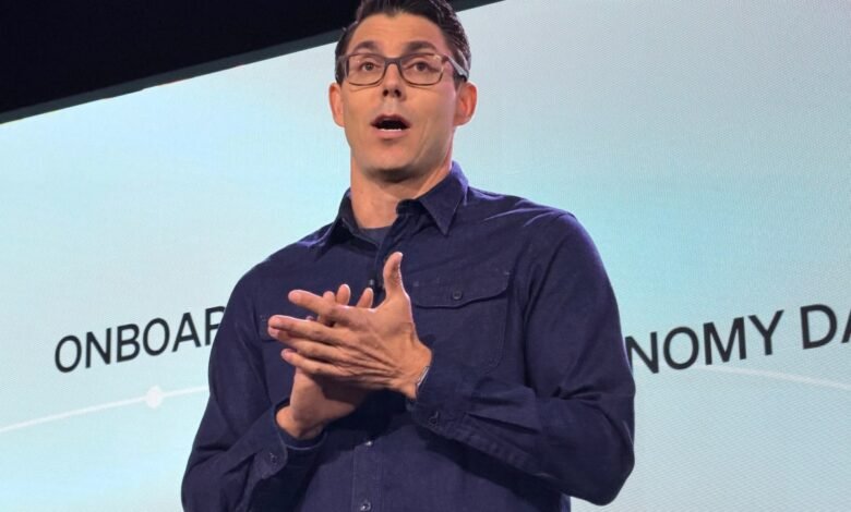 RJ Scaringe, Rivian CEO, presents on stage with hands clasped.