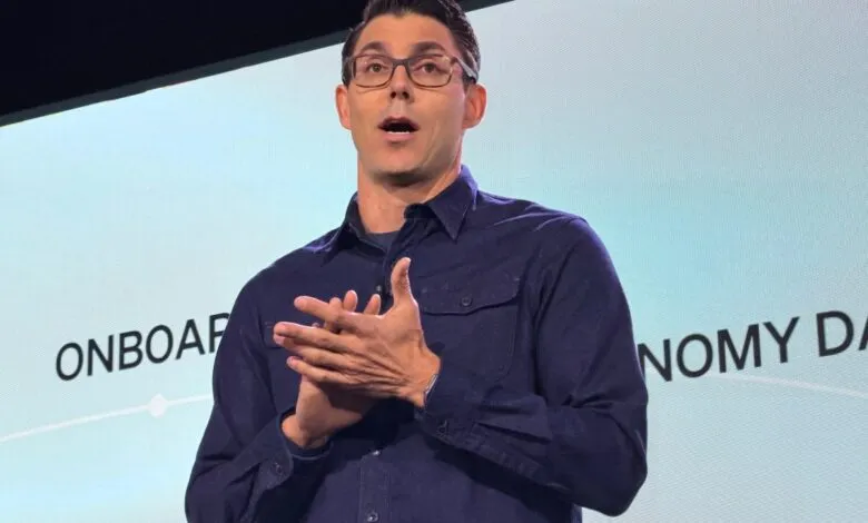 RJ Scaringe, Rivian CEO, presents on stage with hands clasped.