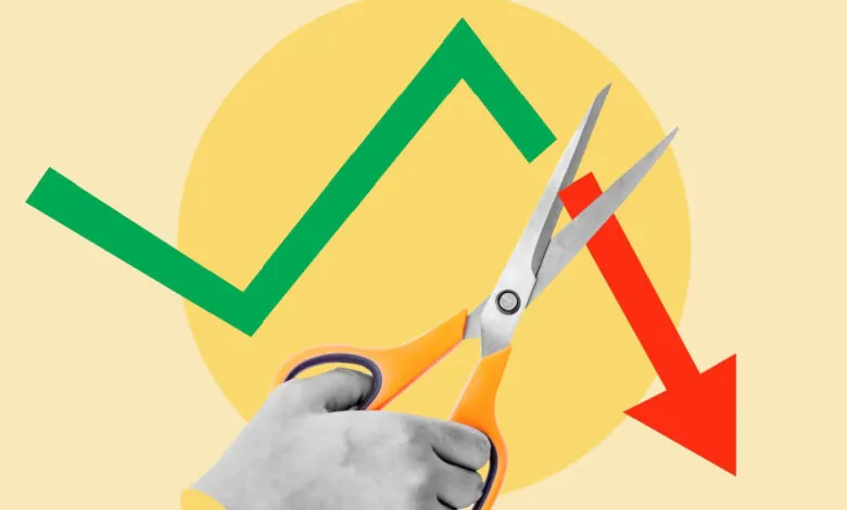Hand with scissors cutting a green upward trend line and a red downward trend line.