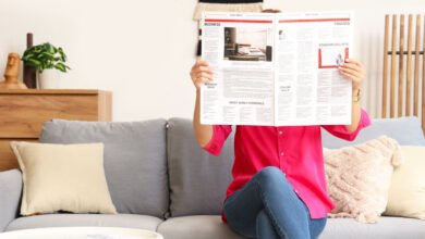 Person reading newspaper on couch, face obscured by paper.