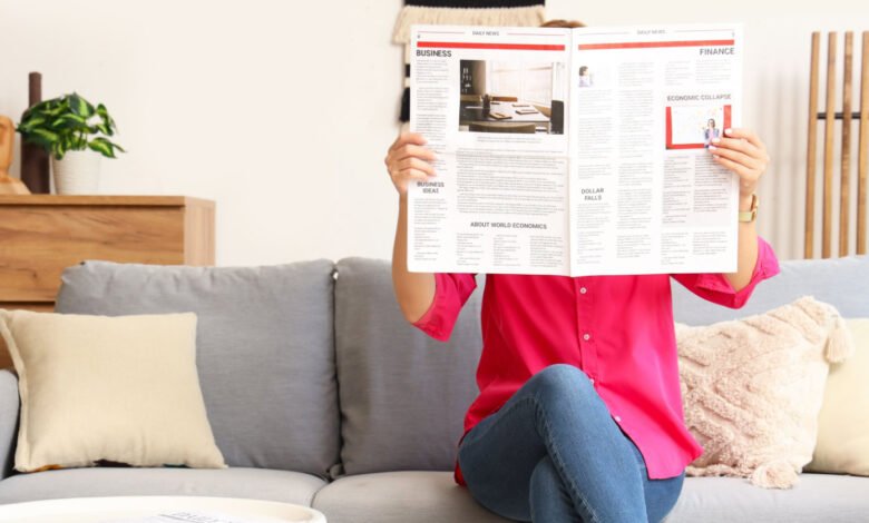 Person reading newspaper on couch, face obscured by paper.