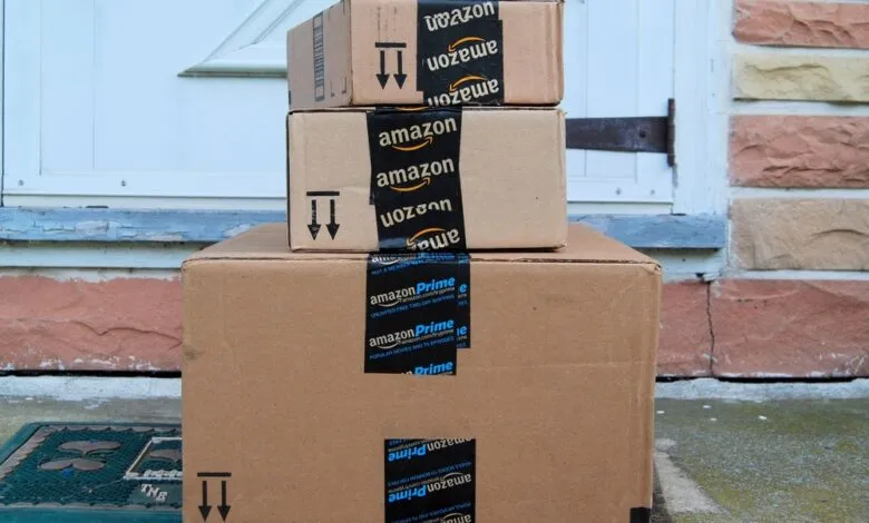 Stack of three Amazon boxes on a porch near a white door.