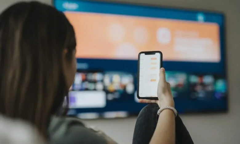 Person using phone while watching TV in living room.